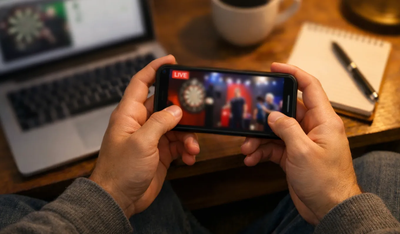 Persoon volgt een live dartswedstrijd op een smartphone terwijl hij een weddenschap plaatst